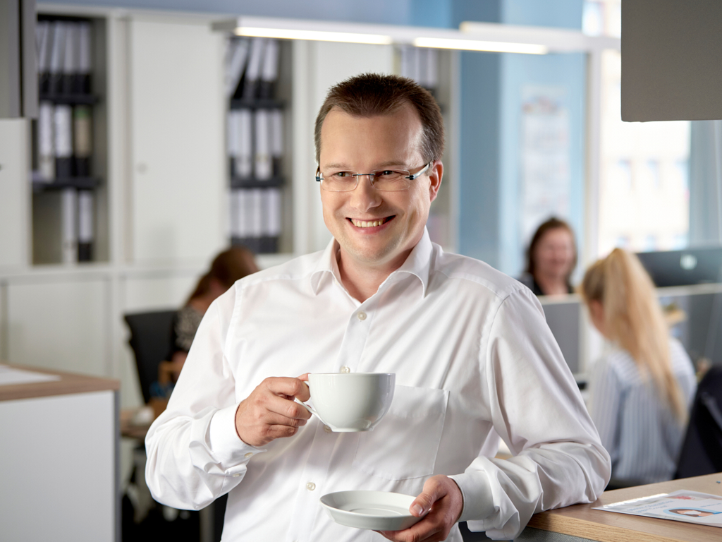 Das Recruiting-Team der apoData freut sich auf Ihre Bewerbung. Ein Mitarbeiter der apoData trinkt lächelnd seinen Kaffee im Büro.