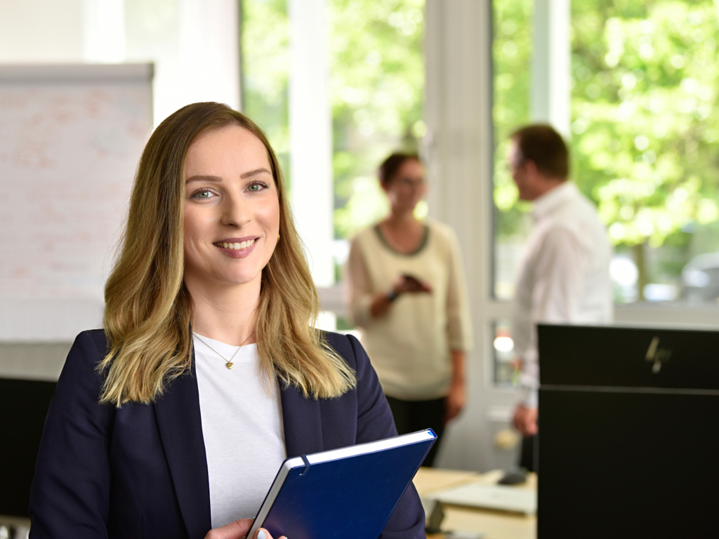 Menschlichkeit und die Chance zur Weiterentwicklung gehören zur Arbeitskultur der apoData. Eine Mitarbeiterin der apoData steht im Büro bei einer Projektbesprechung und lächelt in die Kamera